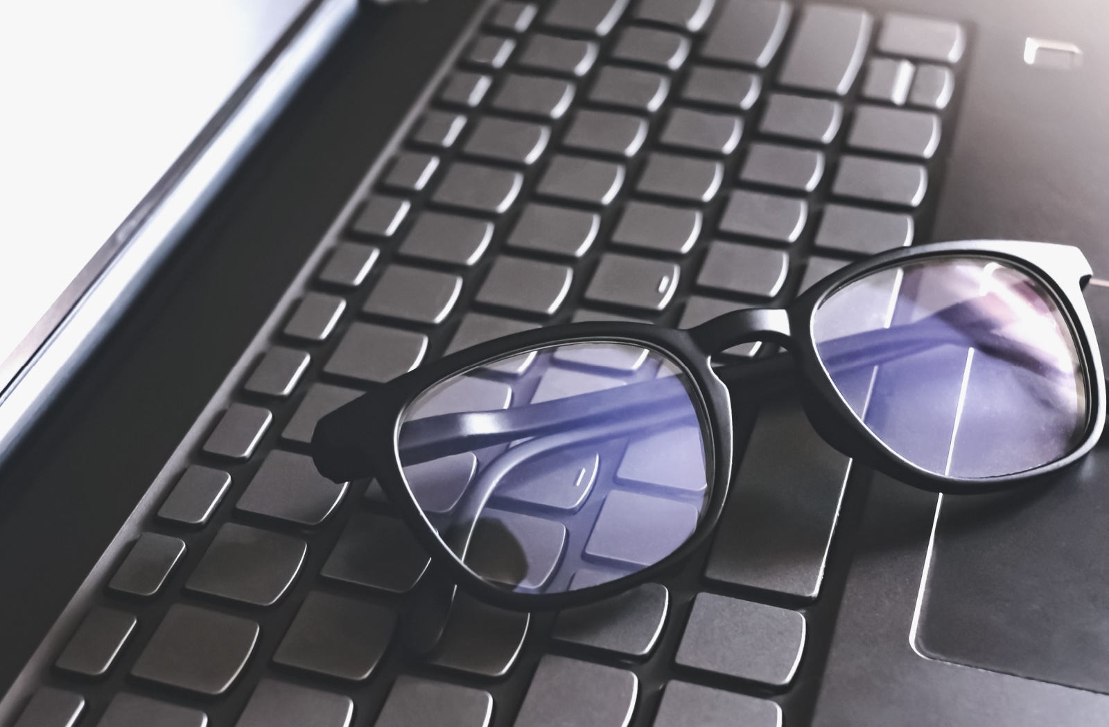 A pair of blue light blocking glasses are balanced on a laptop keyboard.