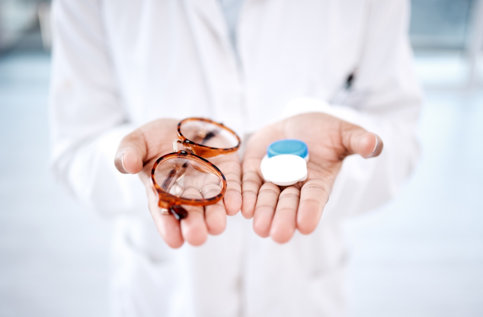 Close-up of an optometrist's hands extending a pair of glasses and a contact lens case.