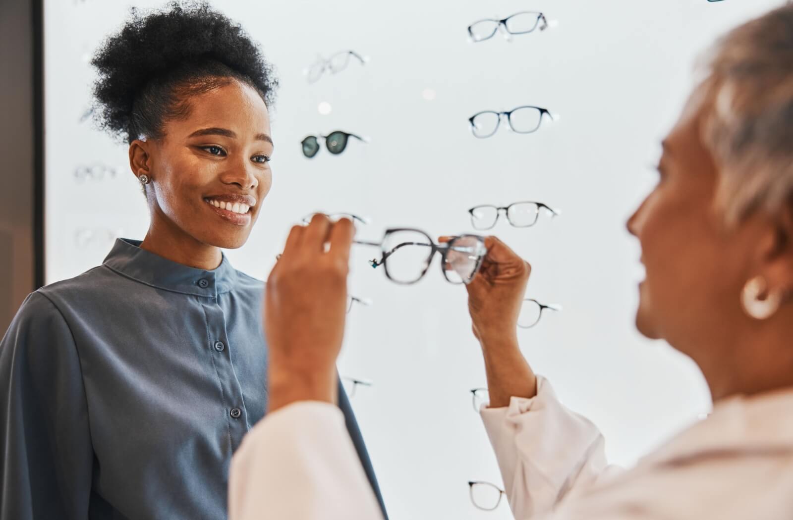 An optometrist holds out a pair of glasses for a patient after an eye exam that determined they needed glasses