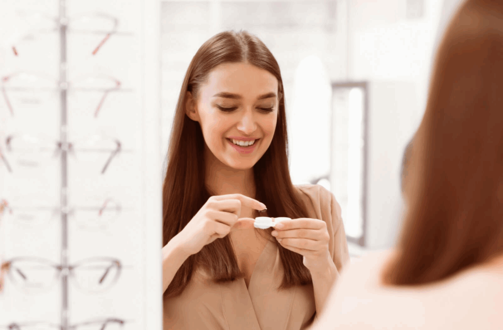 Woman smiling while holding a contact lens near an eyewear display.